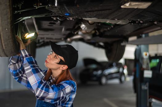 A female mechanic inspects a lifted car. A girl at a man's work