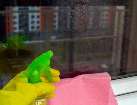 Window washing. In the photo, a hand in a rubber glove sprays from a spray bottle.