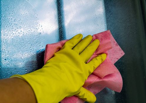 Window washing. In the photo, a hand in a rubber glove with a rag washes a window.