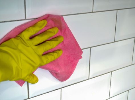 Cleaning. In the photo, a hand in a rubber glove washes the tiles on the wall with a rag.
