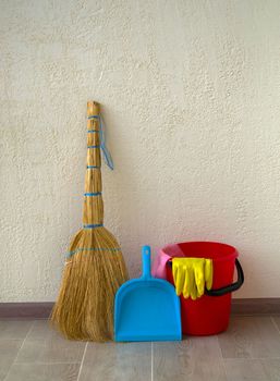 House cleaning. In the photo there is a red bucket, a broom with a dustpan and rubber gloves.