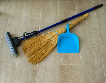 House cleaning. In the photo there is a broom, a mop and a blue dustpan.