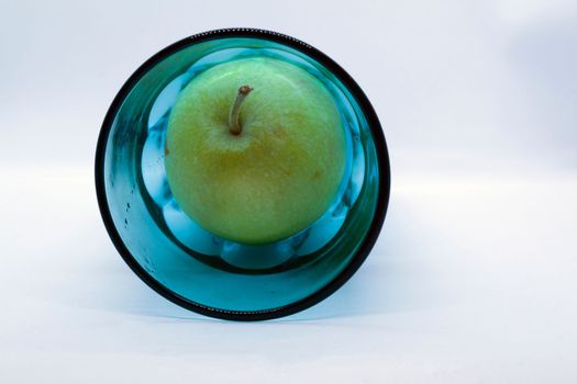 Green apple in a blue glass on a white background close-up.