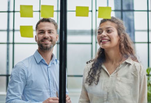 Creative professionals standing and discussing in office behind glass wall with sticky notes