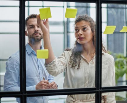 Creative professionals standing and discussing in office behind glass wall with sticky notes