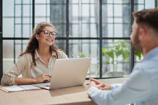 manager in glasses sitting at the table receives a client in the office looking at the camera