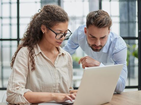 Colleagues check documents using a laptop. A man and a woman are sitting together looking at a laptop. business concept