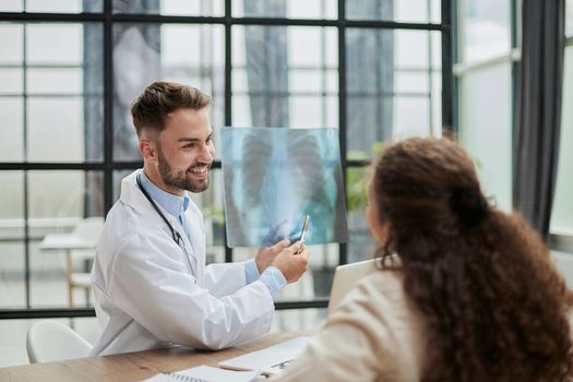 Young serious competent male doctor looking at X-ray at doctor's office