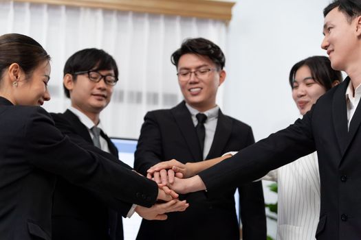 Closeup business team of suit-clad businessmen and women join hand stack together and form circle. Colleague collaborate and work together to promote harmony and teamwork concept in office workplace.