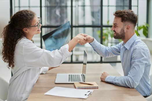 woman doctor holding an x-ray in her hands shakes hands with a patient sitting at a table