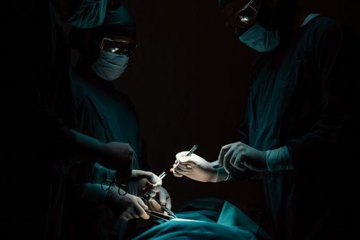 Surgical team performing surgery to patient in sterile operating room. In a surgery room lit by a lamp, a professional and confident surgical team provides medical care to an unconscious patient.