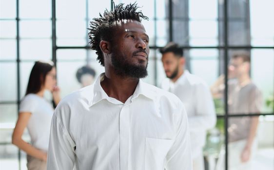 Portrait of smiling African American business man with executives working on laptop in background.