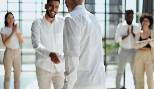 Glad to work with you. Young modern men in smart casual wear shaking hands and smiling while working in the creative office