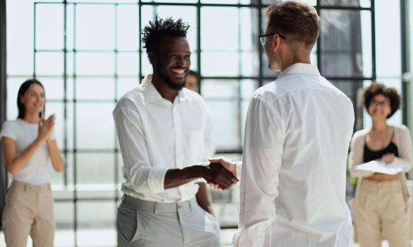 Glad to work with you. Young modern men in smart casual wear shaking hands and smiling while working in the creative office