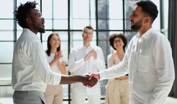 Glad to work with you. Young modern men in smart casual wear shaking hands and smiling while working in the creative office