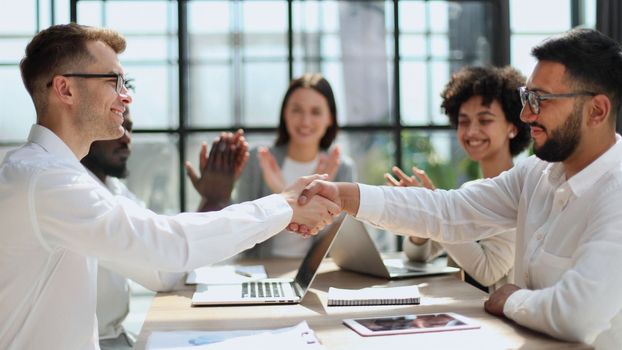 Glad to work with you. Young modern men in smart casual wear shaking hands and smiling while working in the creative office