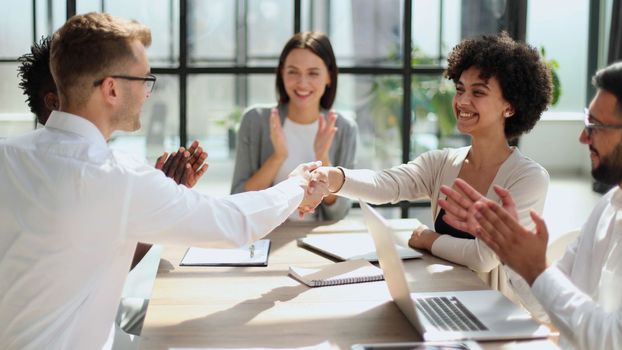 Glad to work with you. Young modern men in smart casual wear shaking hands and smiling while working in the creative office