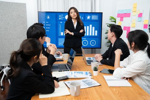 Confidence and young asian businesswoman give presentation on financial business strategy in dashboard report display on screen to colleagues in conference room meeting as harmony in workplace concept