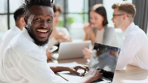 Portrait of smiling African American business man with executives working on laptop in background.