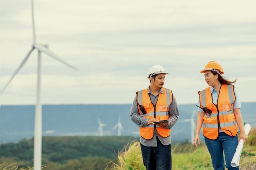 Male and female engineers working on a wind farm atop a hill or mountain in the rural. Progressive ideal for the future production of renewable, sustainable energy.