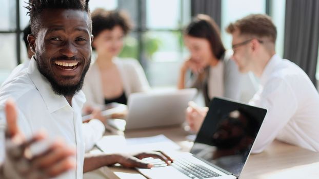 Portrait of smiling African American business man with executives working on laptop in background.