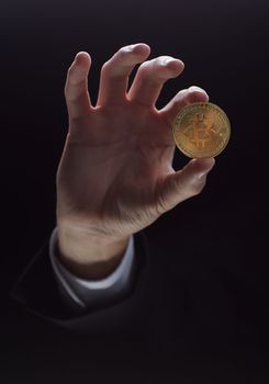 A hand holds a coin isolated on a black background