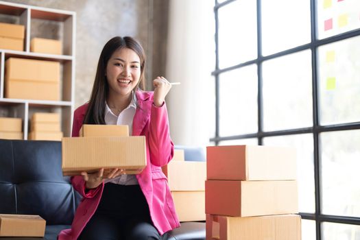 Startup SME small business entrepreneur of freelance Asian woman using a laptop with box Cheerful success happy Asian woman her hand lifts up online
