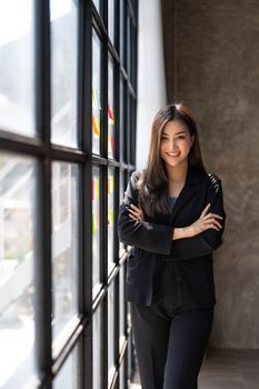 Young business woman standing to drinking coffee and thinking about the strategy of new startup while looking out the window in modern office...