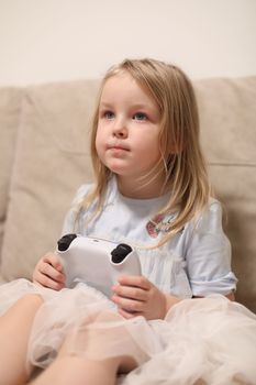 Kids Gaming video games concept. Toddler or young girl playing game with joystick, enjoying games, sitting on sofa in living room at home