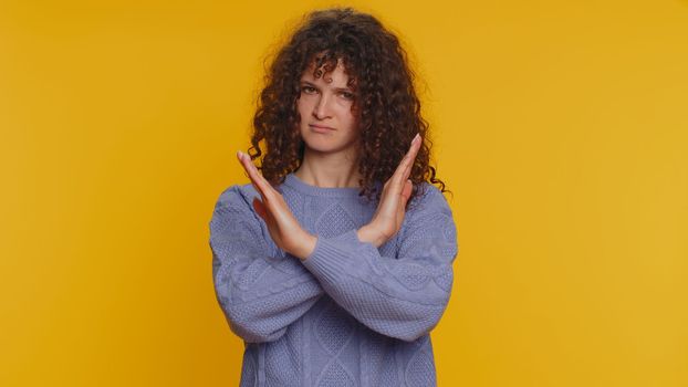 Stop. Curly haired woman say No hold palm folded crossed hands in prohibited access gesture, warning of finish, declining communication, body language danger. Young girl isolated on yellow background