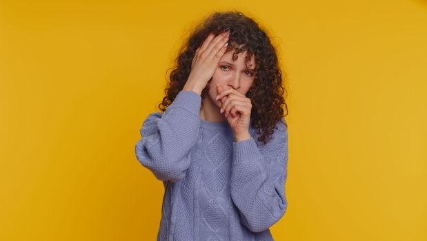 Unhealthy curly haired woman coughing covering mouth with hand, feeling sick, allergy, viral infection symptoms, coronavirus pandemic. Young adult teen girl isolated alone on yellow studio background