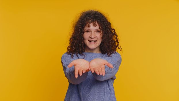 Free gifts and presents for you. Curly haired woman opening hands, glad to see, excitement, preparing surprise, sharing love emotions, congratulating. Young girl isolated on yellow studio background
