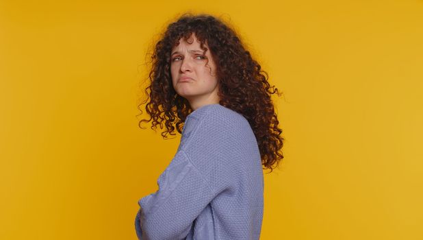 Offended sad curly haired woman having misunderstanding, frustrated after quarrel, ignores and does not want to communicate talk, depression. Young teen girl isolated alone on yellow studio background