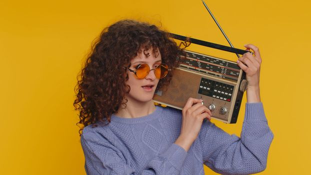 Curly haired woman using retro tape record player to listen music, disco dancing of favorite track, having fun, entertaining, fan of vintage technologies. Young teen girl isolated on yellow background