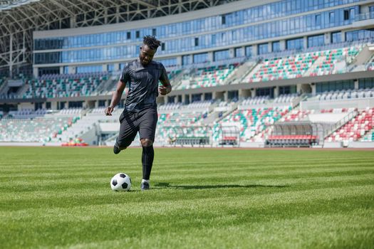 African American man playing football on the stadium field. A man runs with a soccer ball across the field.