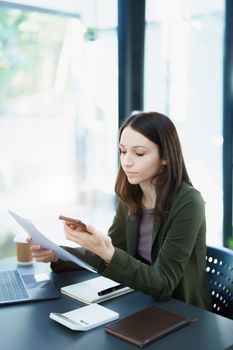 Portrait of a young Asian man showing a smiling face as she uses his phone, computer and financial documents on her desk in the early morning hours.