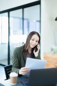 Portrait of a young Asian man showing a smiling face as she uses his phone, computer and financial documents on her desk in the early morning hours.