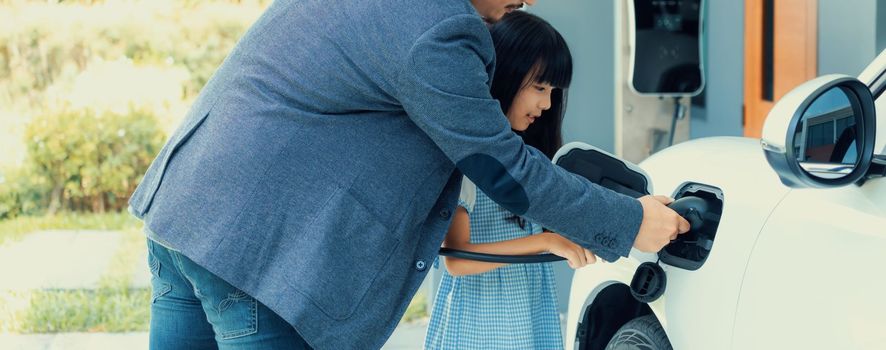 Progressive father and daughter returned from school in electric vehicle that is being charged at home. Electric vehicle driven by renewable clean energy. Home charging station concept for environment