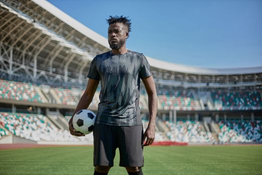 A young man stands in a stadium with a soccer ball in his hand