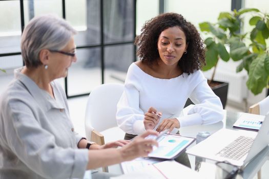 Business women smile while working together on a laptop at a table in the boardroom in the office