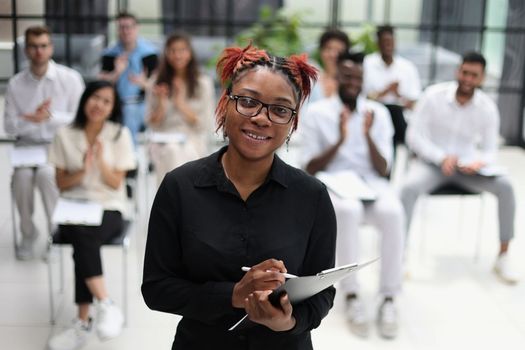 african american woman with a notepad against the background of other people at the seminar. business concept