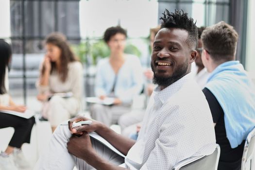 portrait of an African American in a white shirt against the background of his colleagues. looking at the camera