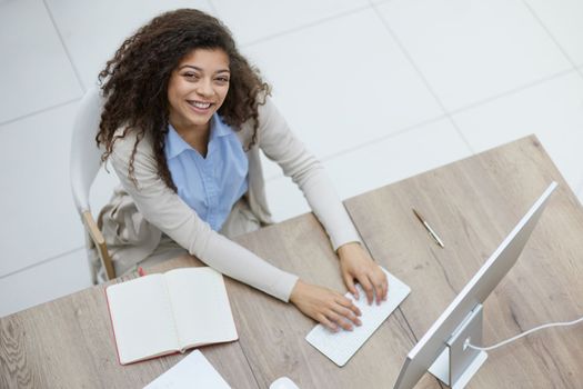 Image of young beautiful joyful woman smiling while working with laptop in office