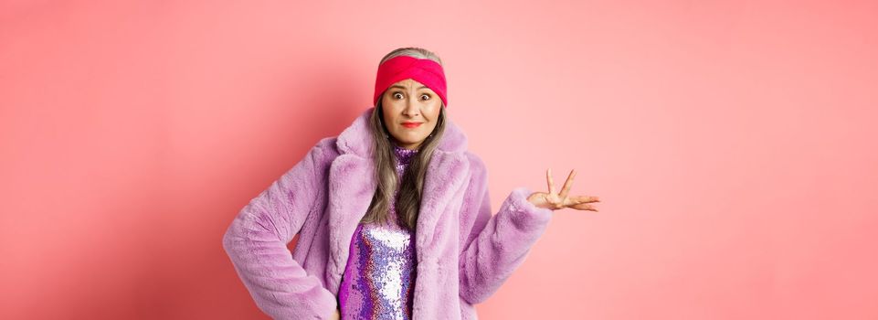 Fashion and shopping concept. Confused senior hipster woman looking puzzled, shrugging with hand spread sideways and clueless stare, standing over pink background.