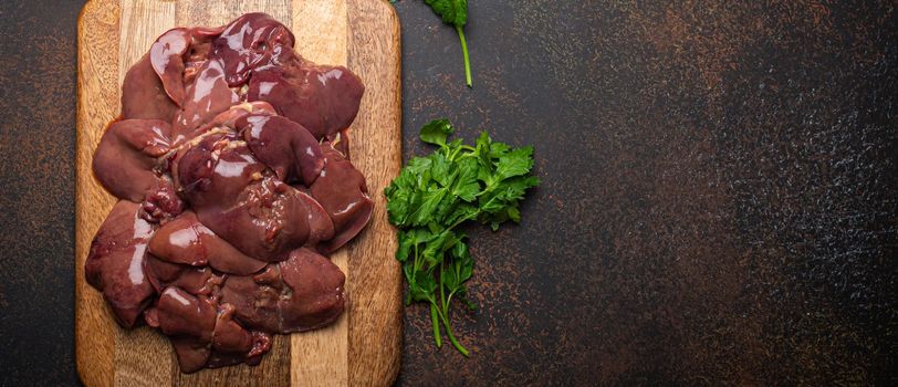 Raw chicken liver on wooden cutting board top view on dark rustic concrete background kitchen table. Healthy food ingredient, source of iron, folate, vitamins and minerals. Space for text