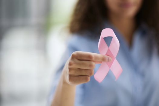 Young woman with pink ribbon smiling happily pointing with hand and finger