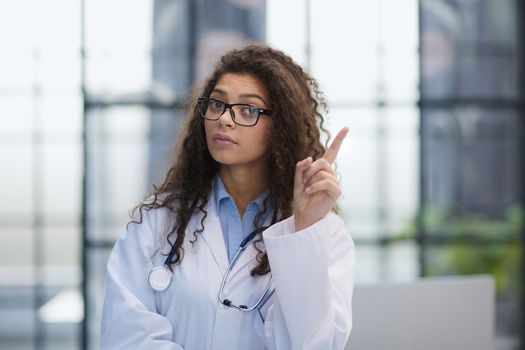 Portrait of an attractive young female doctor in a white coat points her finger