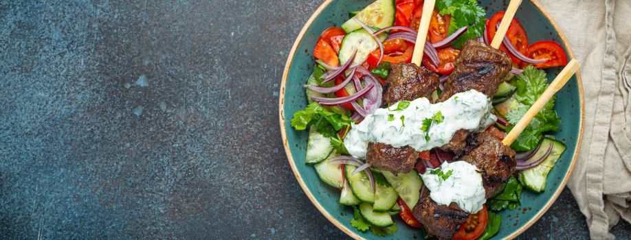 Grilled skewer meat beef kebabs on sticks served with fresh vegetables salad on plate on rustic concrete background from above. Traditional Middle Eastern and Turkish dish Kebab, space for text