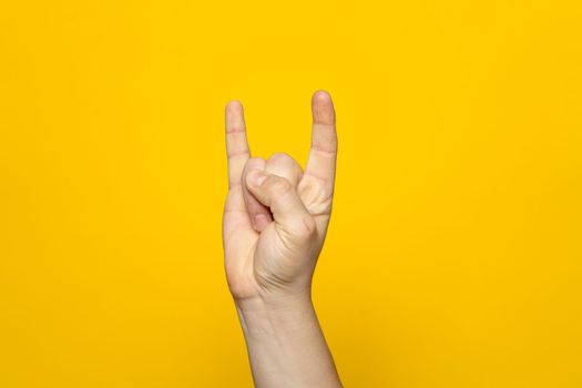 Strong hand of man making the rock gesture on a yellow studio background