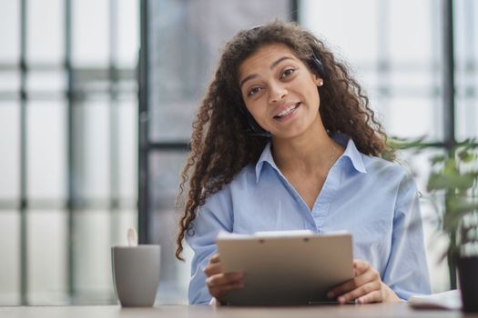 Smiling businesswoman or helpline operator with headset and computer at office